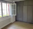 Empty room with wooden flooring, white radiator, grey built-in wardrobe, and large windows with white frames.