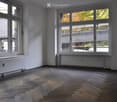 Empty room with wooden flooring, large windows, radiators, and white walls.