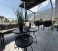 Balcony with a view of mountains, featuring a sofa, tables, chairs, and a potted plant.