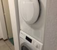 A compact, stacked washing machine and dryer unit in a hallway, with tiled floor and white walls.