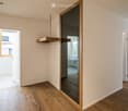 Empty room, wooden floor, mirror, doors on both sides, open door to another room, window on left