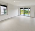 Empty room with white walls, large windows, and sliding glass doors leading to a patio area.