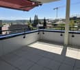Balcony with white tiled floor, black metal railing, and a red retractable awning. Offers a view of a cityscape with buildings and a crane in the distance.