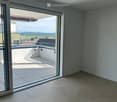Empty room with large sliding glass doors leading to a balcony or terrace area. The floor is tiled, and the walls are painted a neutral gray.