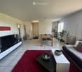 A modern living room with a grey sofa, coffee table, dining table, chairs, television, and decorative items including a plant and vases.
