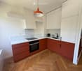 Modern kitchen with white and red cabinets, marble countertops, wooden flooring, and built-in appliances including an oven and induction cooktop.
