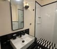 Modern bathroom with black and white tiles, a white sink, a large mirror, and a glass-enclosed shower area.