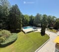 Aerial view of a well-maintained garden area with a large lawn, a swimming pool, lounge chairs, and surrounding trees.