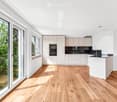 Modern kitchen with light-colored cabinets, wooden flooring, and large windows offering a view of greenery.