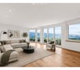 Modern living room with large windows offering a scenic mountain view, featuring a sectional sofa, coffee table, armchair, floor lamp, and decorative plants.