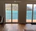 Bright dining area with wooden flooring, large sliding glass doors opening to a wooden deck overlooking a scenic lake and mountains.