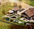 A digital rendering of a residential garden area with a house, patio, trampoline, and outdoor furniture.