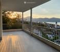 Balcony with a scenic view of a town, lake, and mountains during sunset.
