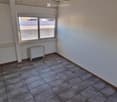 Empty room with tiled floor, white walls, a single window, and a radiator. No furniture or equipment present.