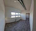 Empty room with tiled floor, white walls, large windows, radiator, and a door leading to another space.
