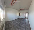 Empty room with tiled floor, white walls, and a large window with blinds. There is a door leading to another space.