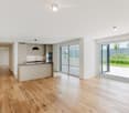 Modern, open-plan kitchen and living area with light wooden flooring, white walls, and large sliding glass doors leading to an outdoor space.