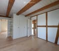 Empty room with wooden flooring and white walls, featuring exposed wooden beams on the ceiling and built-in white closet units.