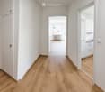 Empty hallway with wooden flooring, white walls, and doors leading to other rooms.