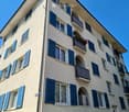Four-story building with light beige facade, blue shutters, and multiple balconies with flower boxes.