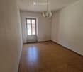 Empty room with wooden flooring, light-colored walls, and a single window with a radiator below it. A chandelier hangs from the ceiling.