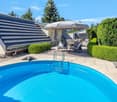 Outdoor area with a swimming pool, lounge chairs, umbrella, dining table, and surrounding greenery.