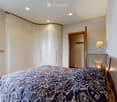Modern bedroom with a large bed, sleek white wardrobe, nightstand with a lamp, and recessed ceiling lighting.