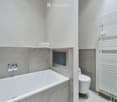 Modern bathroom with a bathtub, toilet, towel rack, and neatly folded towels on a shelf.