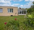 A well-maintained garden with a lawn, colorful flowers, and a modern house with large windows and a covered patio area.