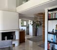 Modern living room with a grey sofa, bookshelf, fireplace, and a small kitchen area visible in the background.