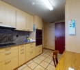 Bright kitchen with light wooden cabinets, granite countertop, and a small dining area with a wooden table and chair. A bottle and cup are placed on the counter.