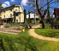 A well-maintained garden with a lawn, pathways, potted plants, and several residential buildings in the background.
