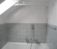 Bathroom with white bathtub, gray tiles, white ceiling, shower head, and faucets