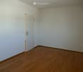 Empty room with light-colored walls and wooden flooring, featuring a single white door leading to another space.