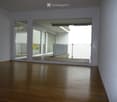 Empty room with wooden flooring, large sliding glass doors leading to a balcony area, white walls, and a metal safety barrier visible on the balcony.