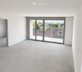 Empty room with white walls, concrete floor, large sliding glass doors leading to a balcony, and an open doorway to another space.