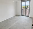 Empty room with white walls and a concrete floor, featuring a large sliding glass door leading to a balcony with a view of the landscape.