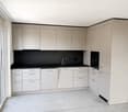 Modern kitchen with light-colored cabinets, white lower units, black countertop, and a single sink with a modern faucet.