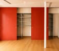 Empty room with wooden flooring, beige walls, and built-in storage units with red panel doors.