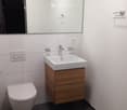 Modern bathroom with white tiles, dark floor, wooden cabinet under sink, large mirror, and toilet.