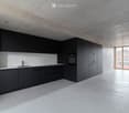 Modern kitchen with sleek black cabinets, a stainless steel sink, and built-in oven. The space features a minimalist design with concrete floors and walls.