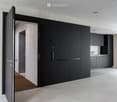 Modern hallway with a large open door leading to a kitchen area, featuring sleek black cabinetry and a minimalist design.
