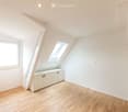 Bright, empty attic room with wooden flooring, white walls, built-in cabinetry, and skylight windows.