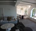 Bright living room with a sofa, coffee table, dining table, and chairs. Large arched windows and a hanging lamp provide natural light.