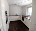 Modern kitchen with white cabinets, dark brown countertops, and a dark tiled floor. Features a sink, faucet, and built-in oven.