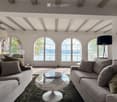 Modern living room with large arched windows offering a scenic view, featuring two grey sofas, a glass coffee table, and floor lamps.