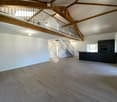 Open-plan space with wooden beams, a staircase leading to an upper level, and a modern kitchen area with dark cabinets and a countertop.