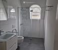 modern bathroom with white tiles, glass shower enclosure, white sink, white toilet, mirror, power outlet