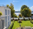 Well-maintained garden with green lawn, small trees, shrubs, and a view of a lake and surrounding landscape.