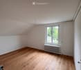 Empty room with wooden flooring, white walls, and a window with a radiator below it. The ceiling is slanted, typical of an attic space.